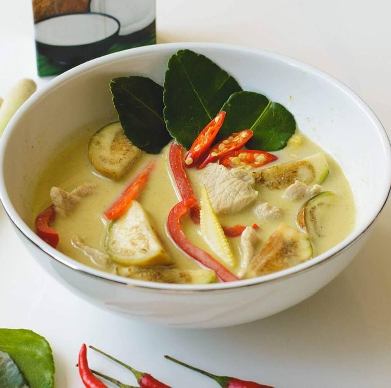Kremet thaisuppe med kylling, grønnsaker, chili og kaffir limeblader i en hvit bolle.