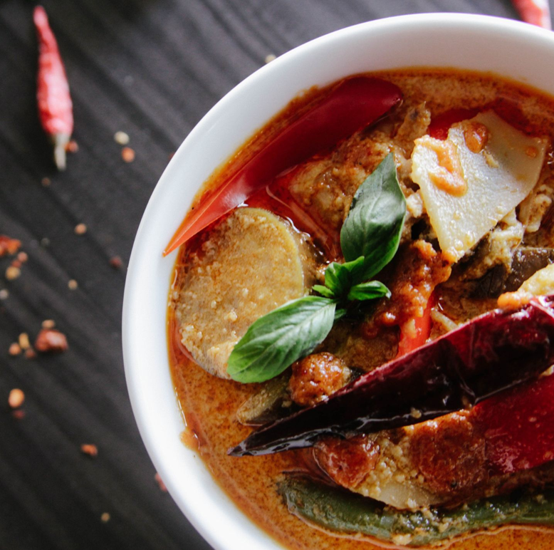 En bolle med krydret curry, grønnsaker og chili, dekorert med basilikumblader på en mørk bakgrunn.