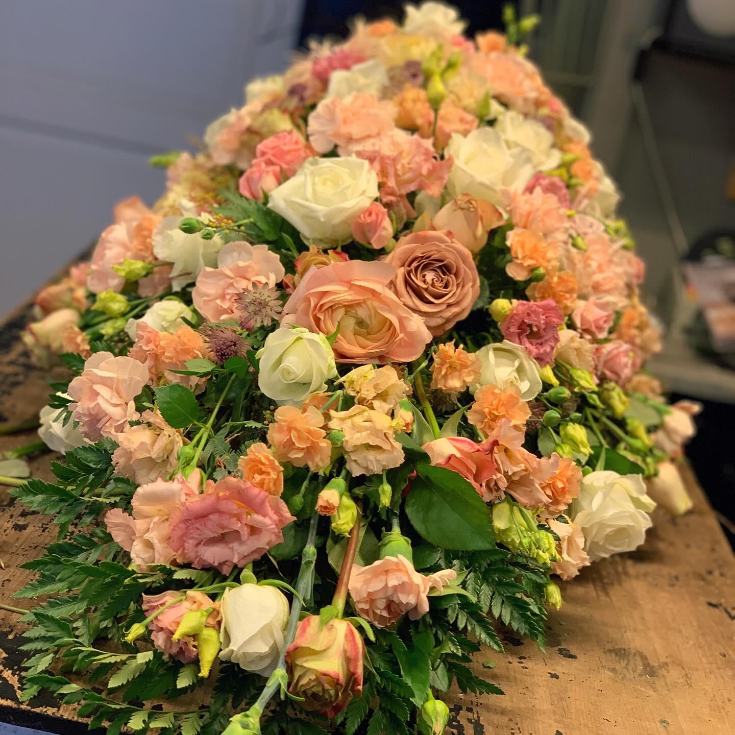 En vakker blomsteroppsats med rosa og hvite roser, nelliker og grønt, plassert på en treflate.