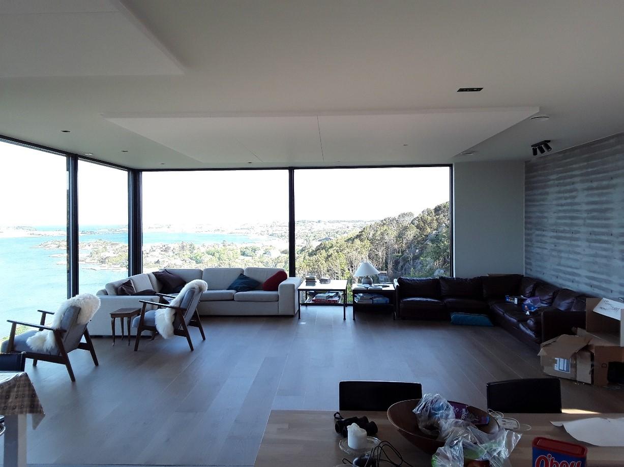 Moderne stue med store vinduer, utsikt over havet, sofa, stoler og et spisebord.
