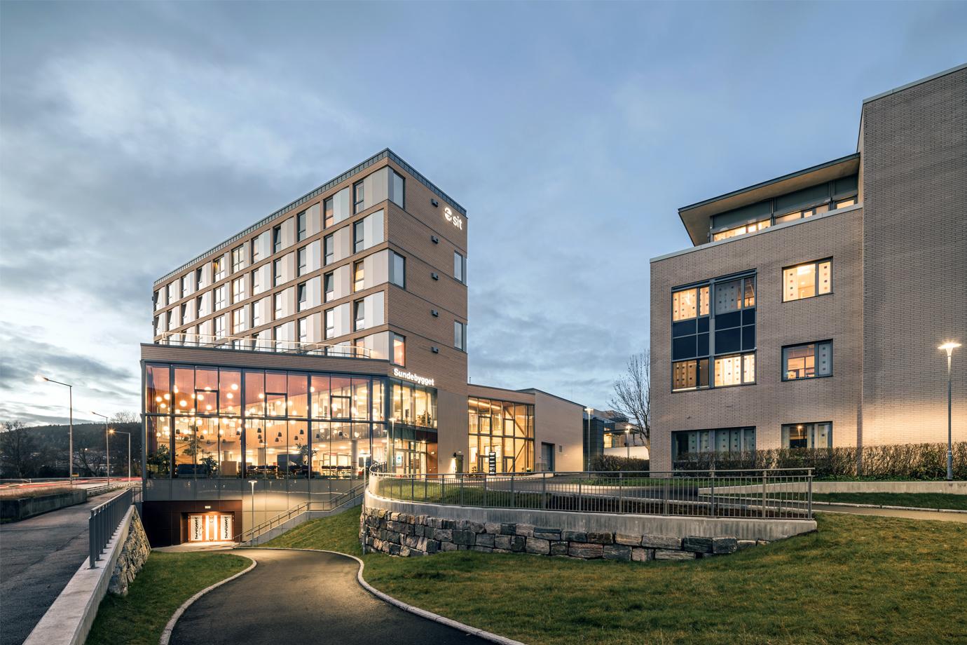 Moderne hotellbygning med glassfasade og tilknyttede bygninger i en urban setting ved skumring.