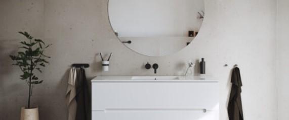 Moderne bad med rund speil, hvit servant, planter og håndklær på veggen. Minimalistisk design og nøytrale farger.