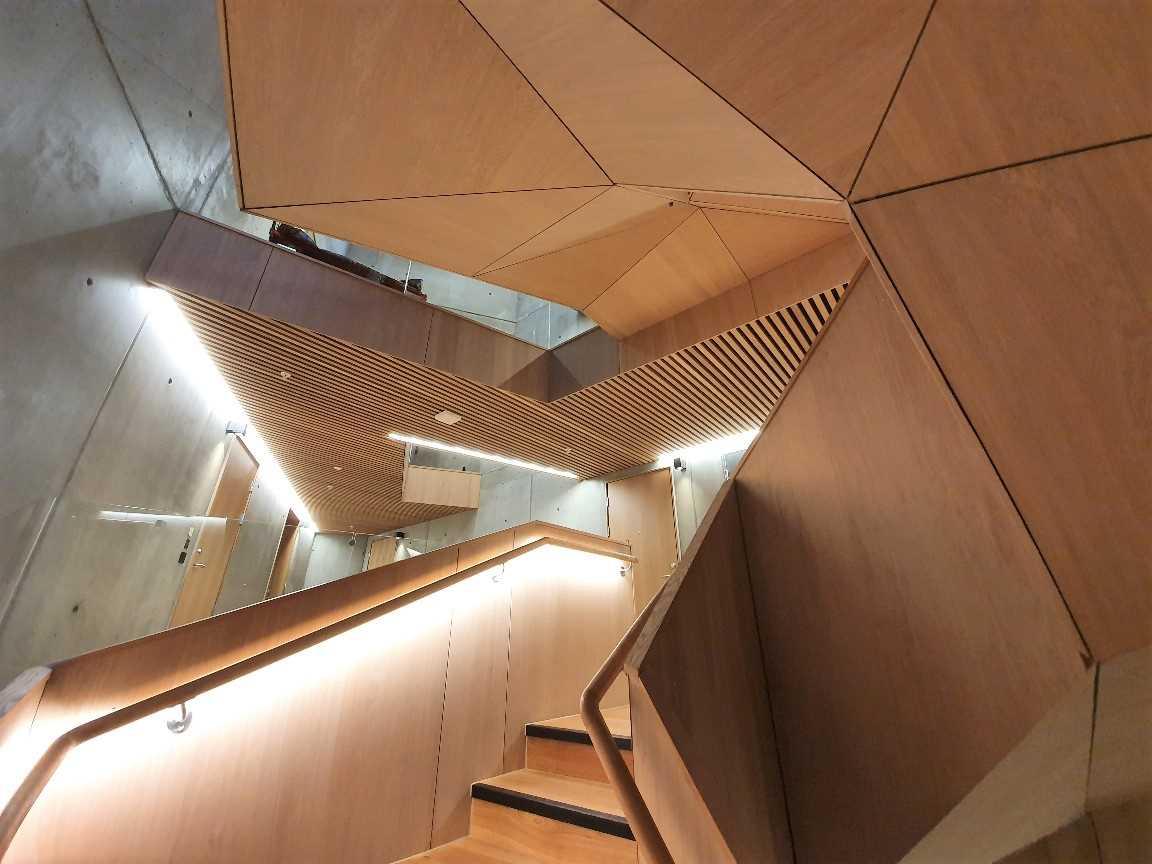 Moderne trapp med geometrisk design og trepanel, belyst av LED-lamper i en moderne bygning.