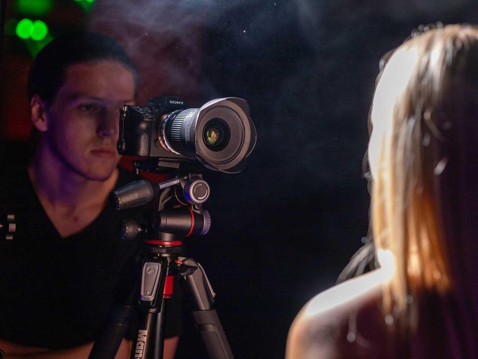 En fotograf med kamera på stativ tar bilder av en modell i et røykfylt rom.