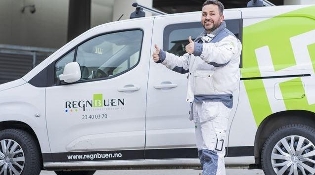 En smilende mann i arbeidsklær gir tommel opp ved siden av en hvit varebil med logoen til Regnbuen.