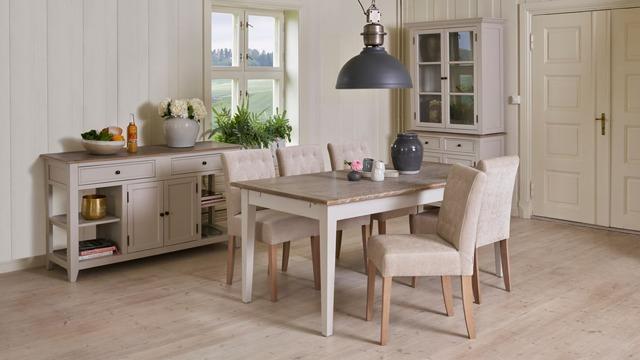 Moderne spisestue med et lyst bord, stoler i beige stoff og en stor lampe over bordet, samt en hylle og skap.