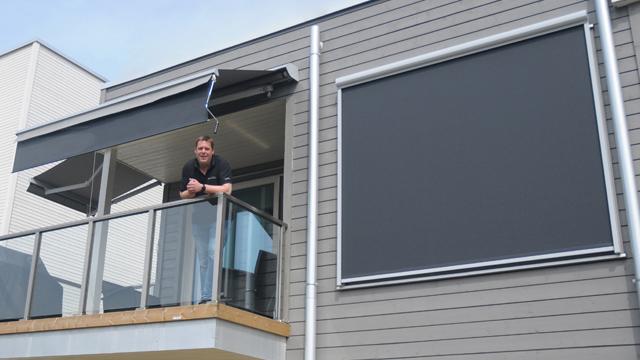 En mann står på balkongen i en moderne bygning med markiser som gir skygge.