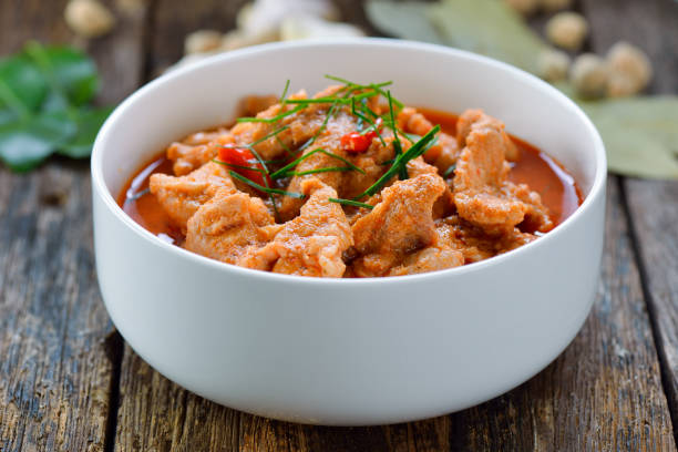 En hvit bolle med kjøttgryte, toppet med urter og chili, servert på et trebord.