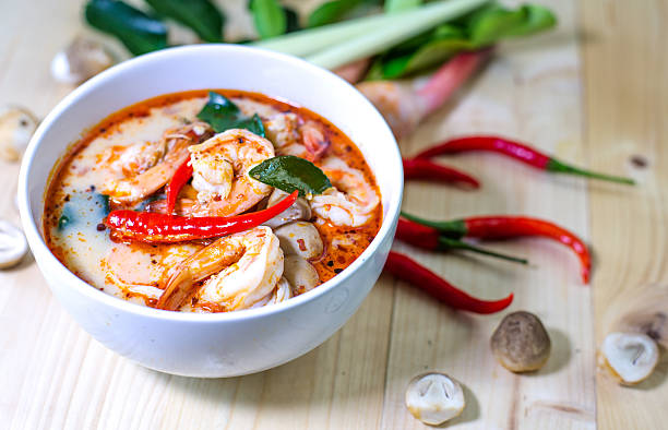 En bolle med tom yum suppe med reker, chili, sitrongress og kaffir limeblader på et trebord.