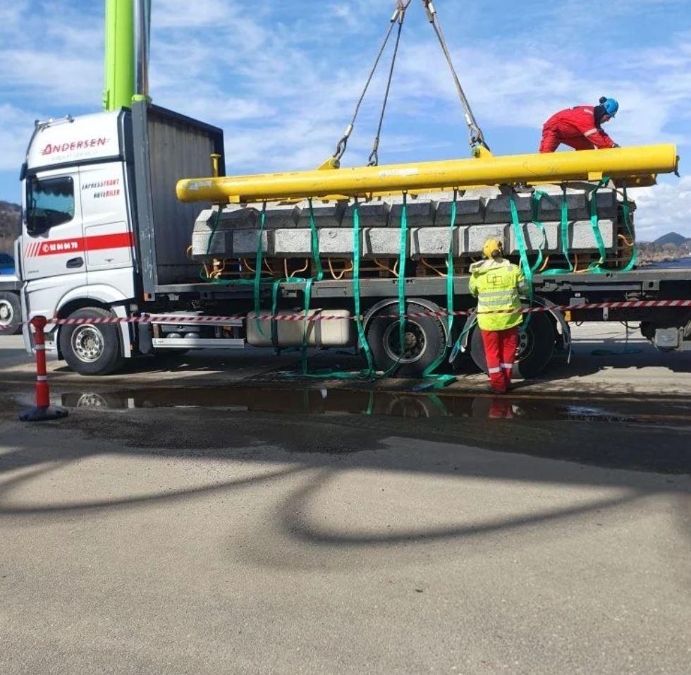 Lastebil med kran som løfter en stor betongstruktur, mens arbeidere overvåker prosessen.
