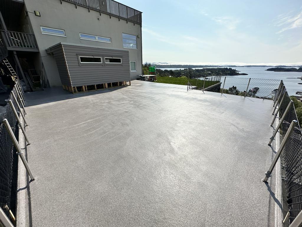 Utsikt over en stor, ny betongterrasse med rekkverk og sjø i bakgrunnen.