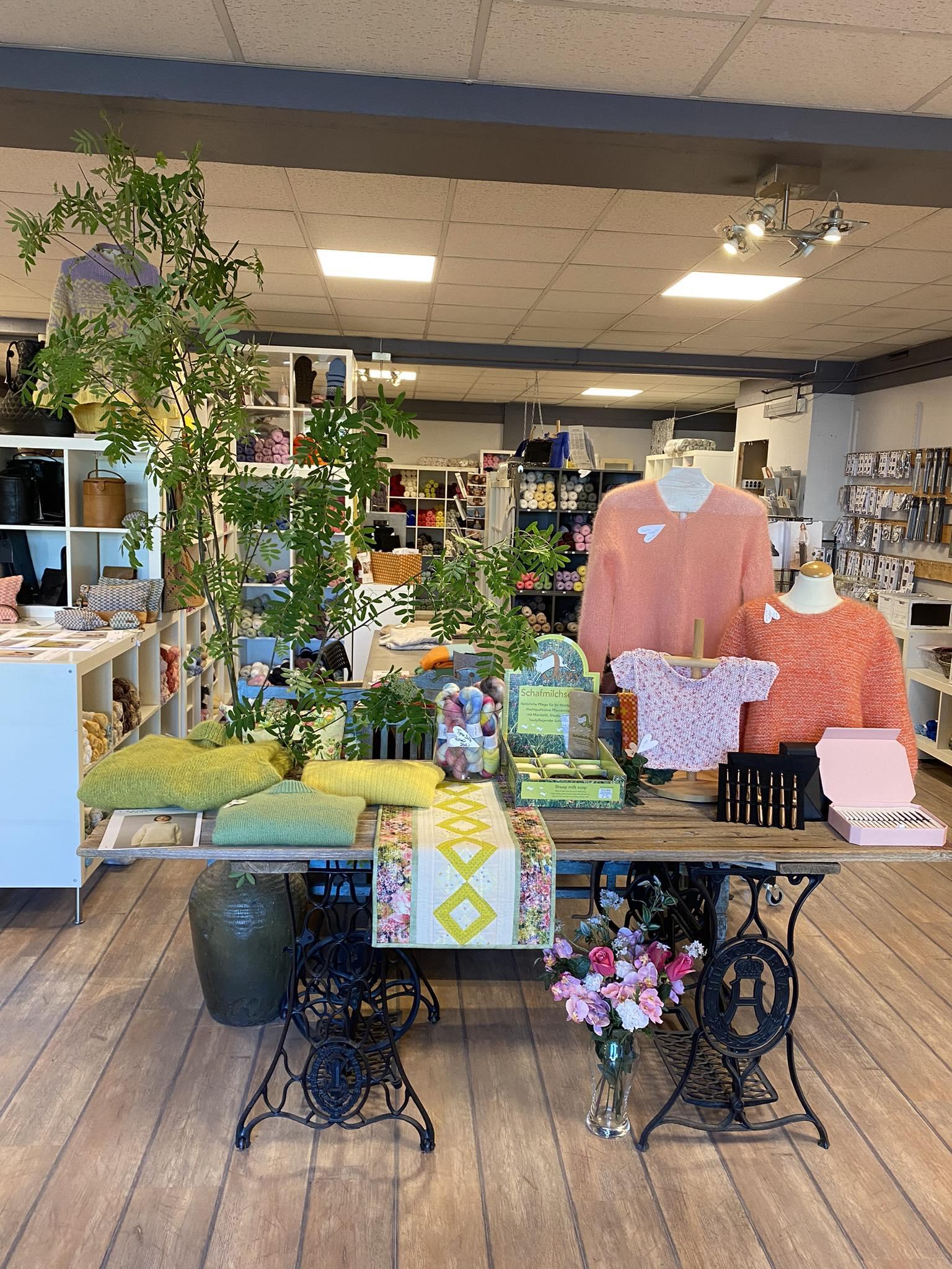 En butikkinnredning med klær, planter og dekorative gjenstander på et bord i en lys og moderne atmosfære.
