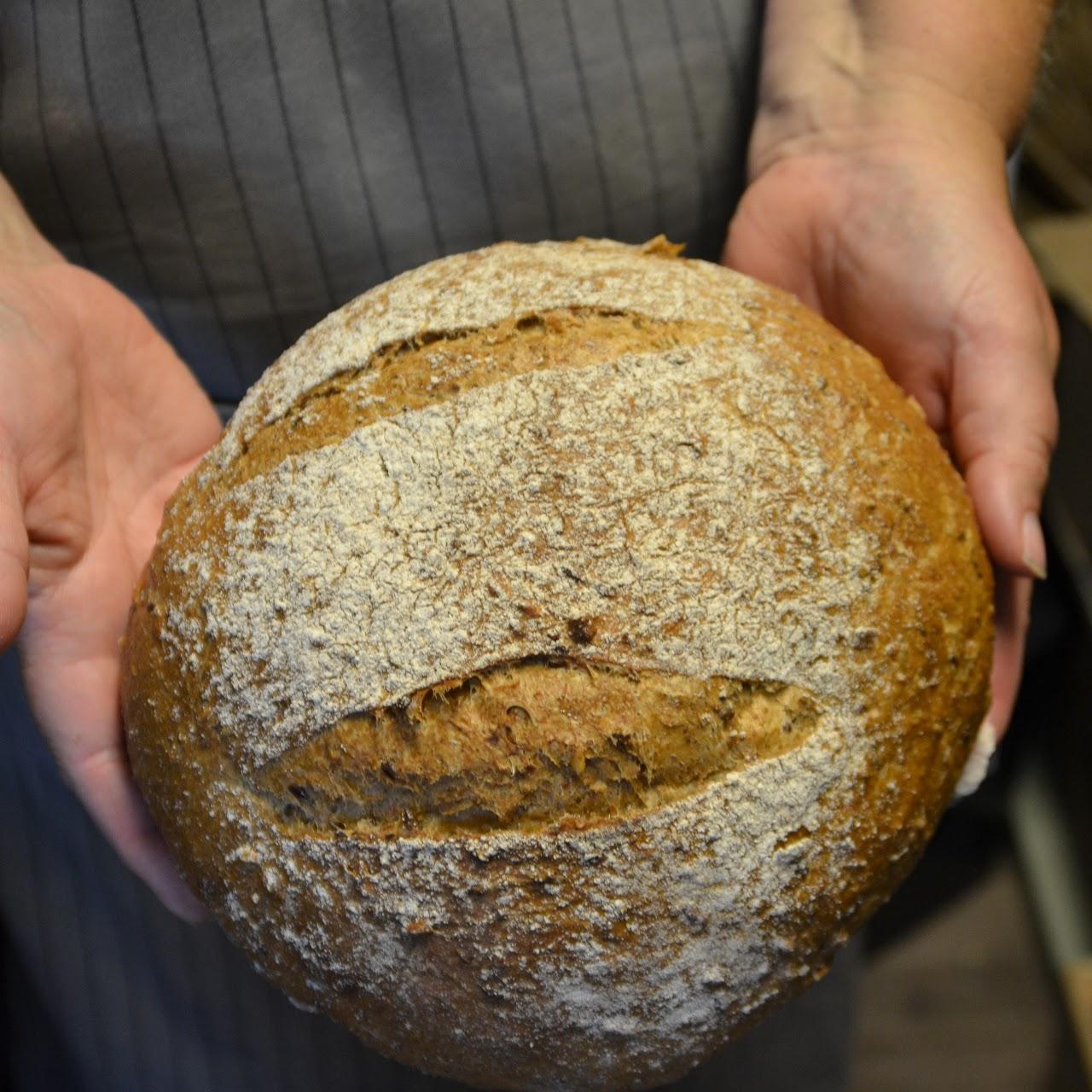 Hender som holder et nybakt, rundbrød med sprø skorpe og melstøv på overflaten.