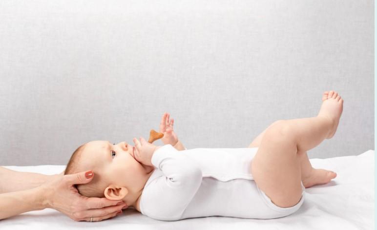En baby ligger på ryggen med en hånd som støtter hodet, og suger på en smokk.