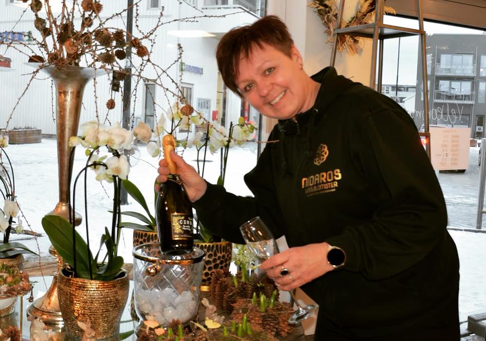 Kvinne som heller champagne i et glass ved en dekorert bord med blomster og is.