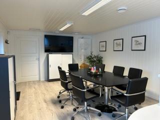 Moderne møterom med et stort bord, svarte stoler, TV-skjerm og kunstverk på veggene.