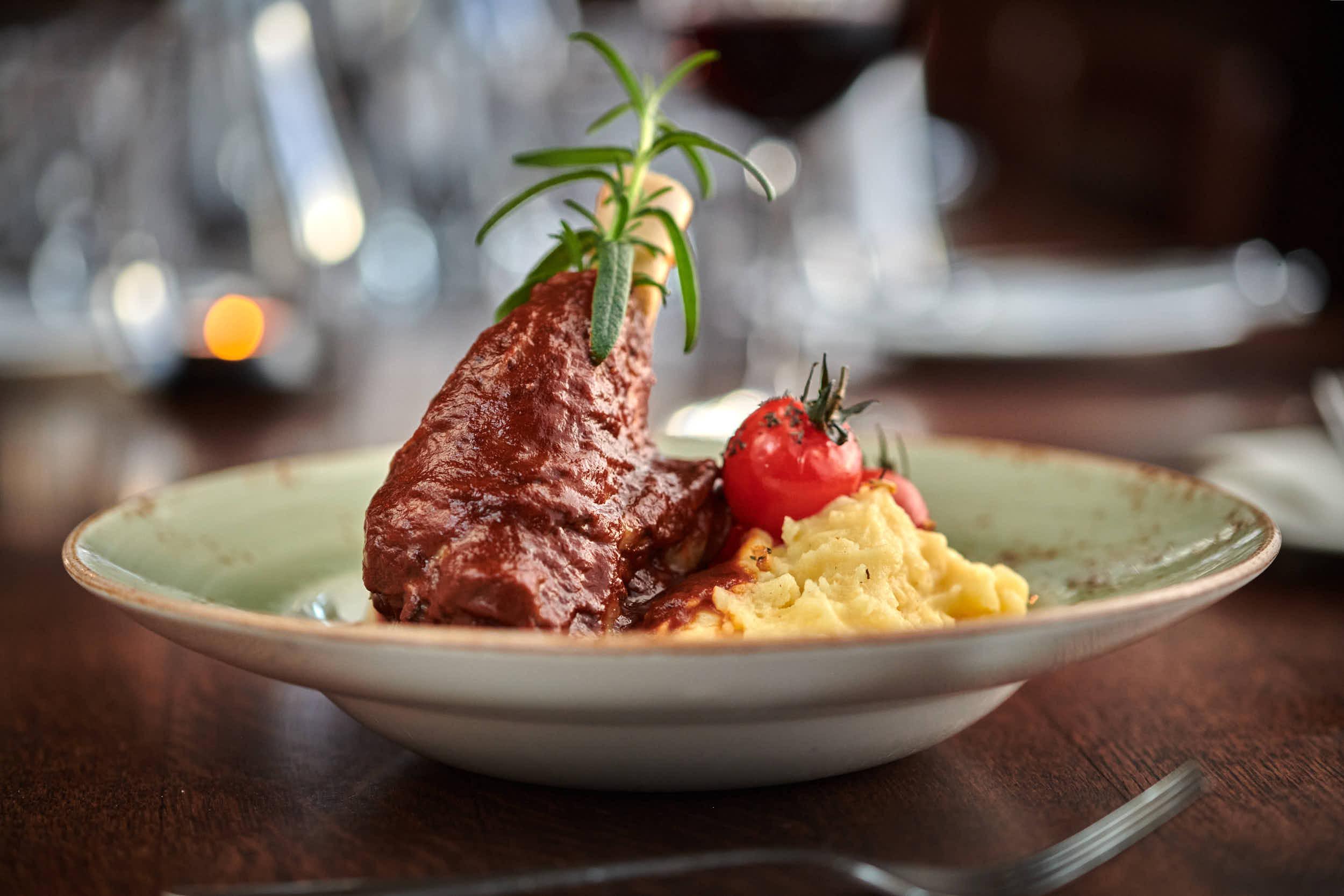 En tallerken med saftig kjøtt, potetmos og en cherrytomat, dekorert med urter.