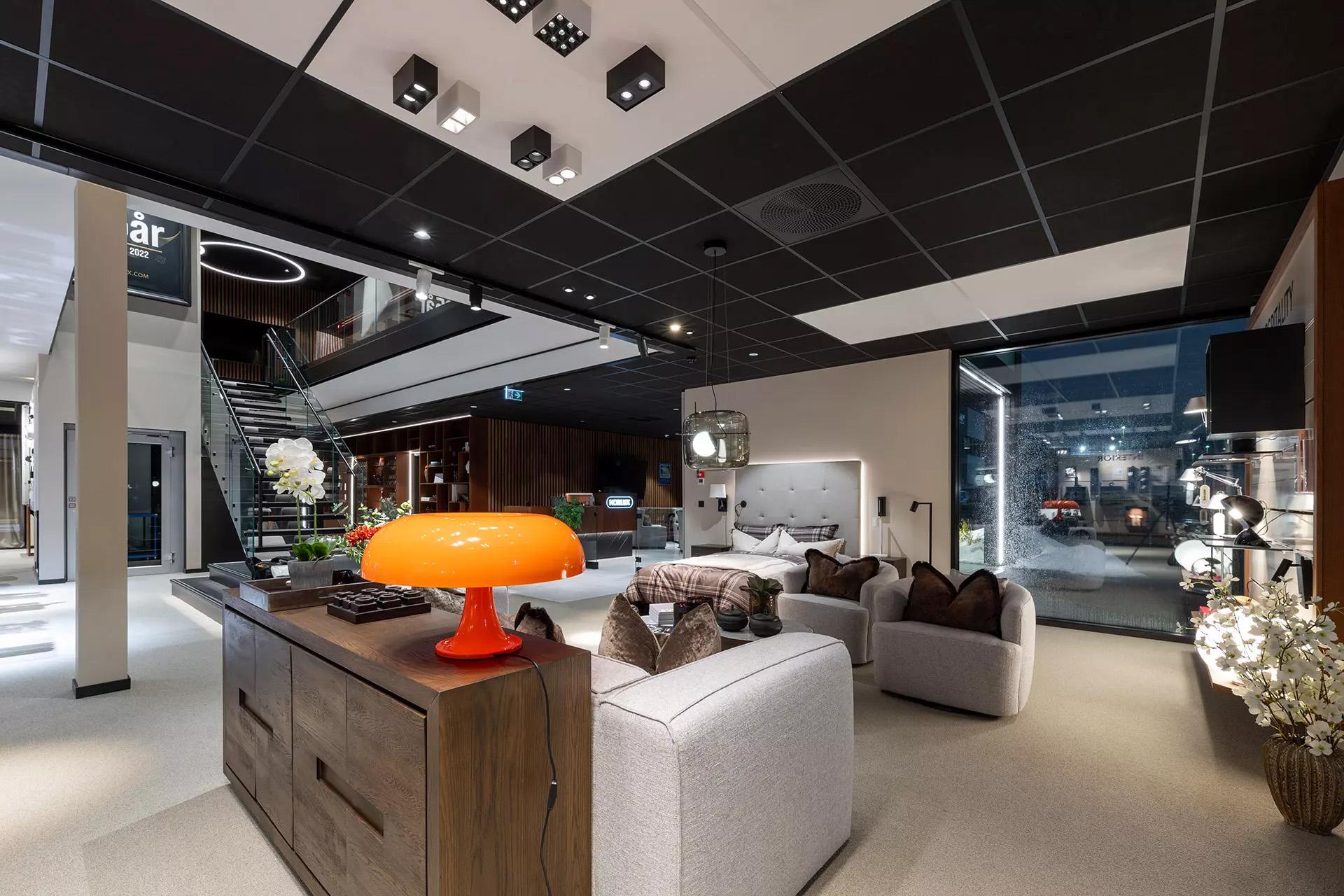 Moderne stue med en lys oransje lampe, sofa, og stilige møbler, samt en åpen trapp i bakgrunnen.