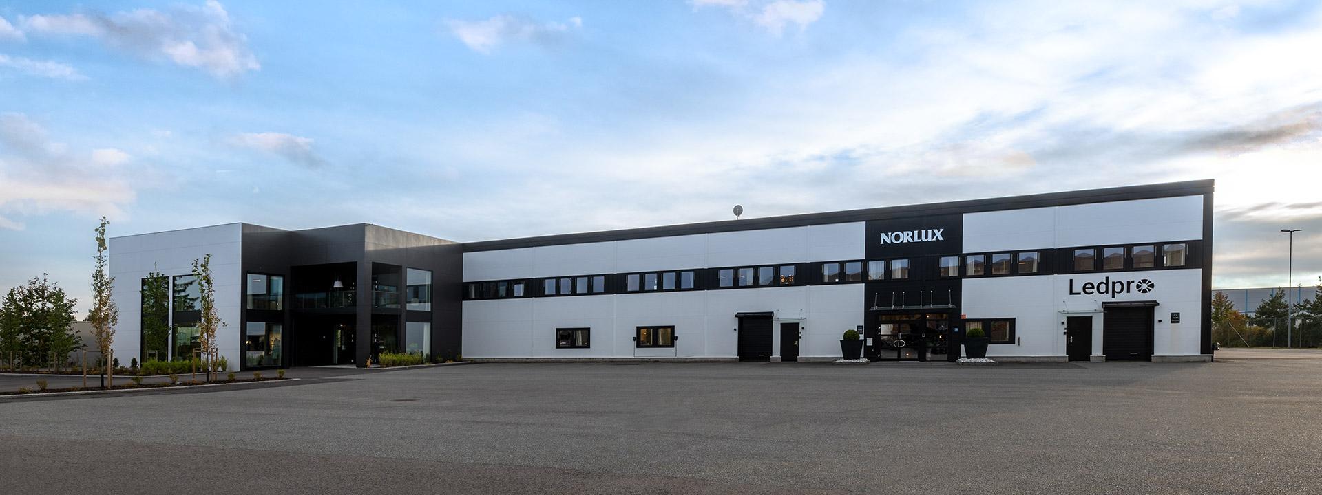 Moderne hotellbygning med hvit og svart fasade, parkering foran og trær på siden.