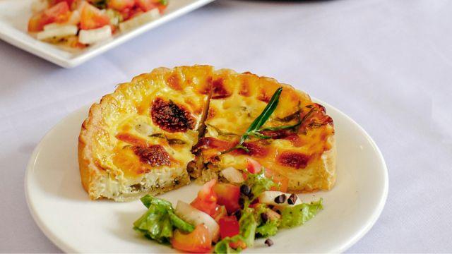 En tallerken med en skive quiche og en frisk salat med tomater og grønne blader.