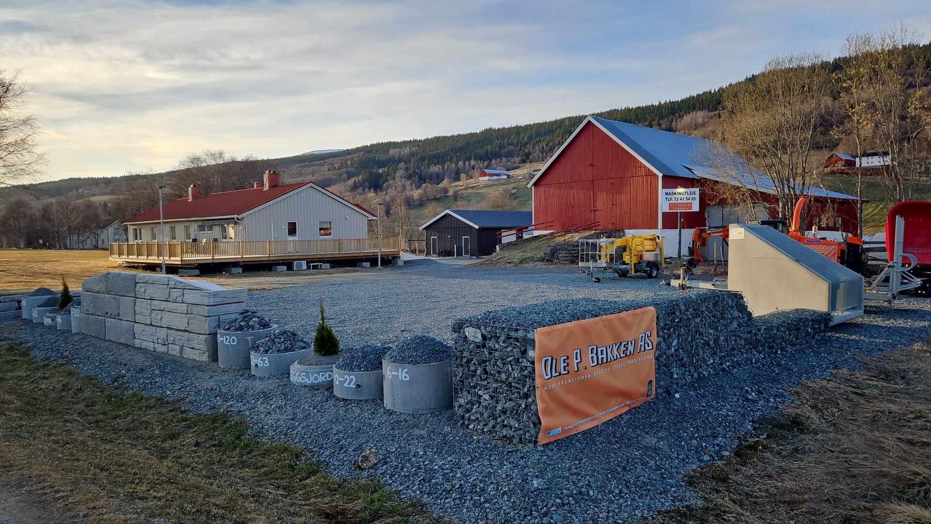 Byggeplass med grus, steinblokker og bygninger i bakgrunnen under en klar himmel.