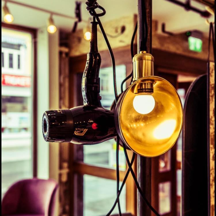 Hårføner hengende ved siden av en gyllen lampe i en moderne frisørsalong.