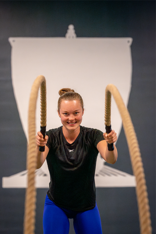 Kvinne som trener med tau i et treningsstudio, smilende og fokusert på øvelsen.