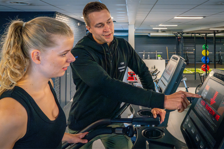 Trener viser en kvinne hvordan man bruker treningsutstyr på et moderne treningssenter.