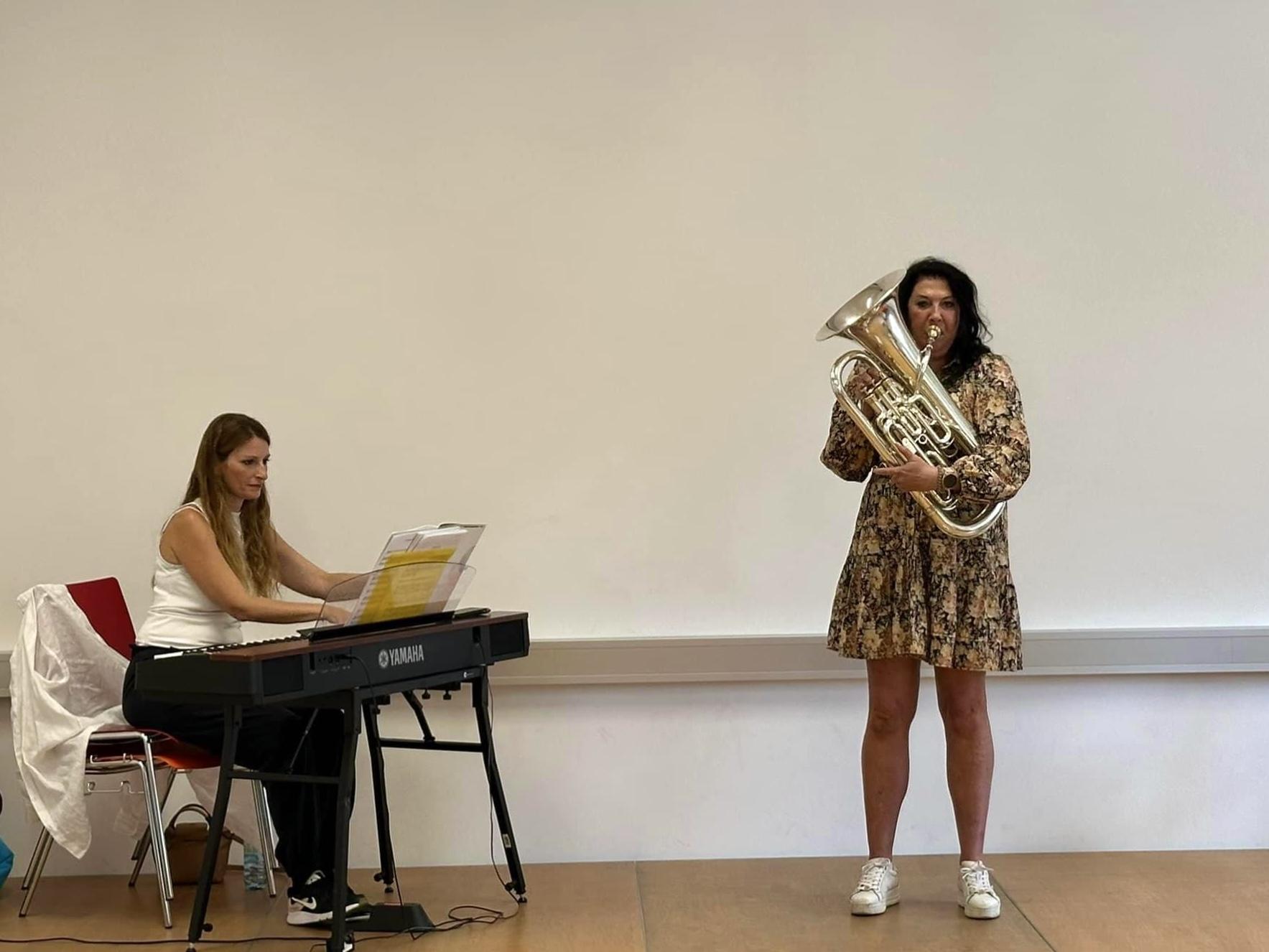 En kvinne spiller tuba mens en annen kvinne spiller piano på en scene.