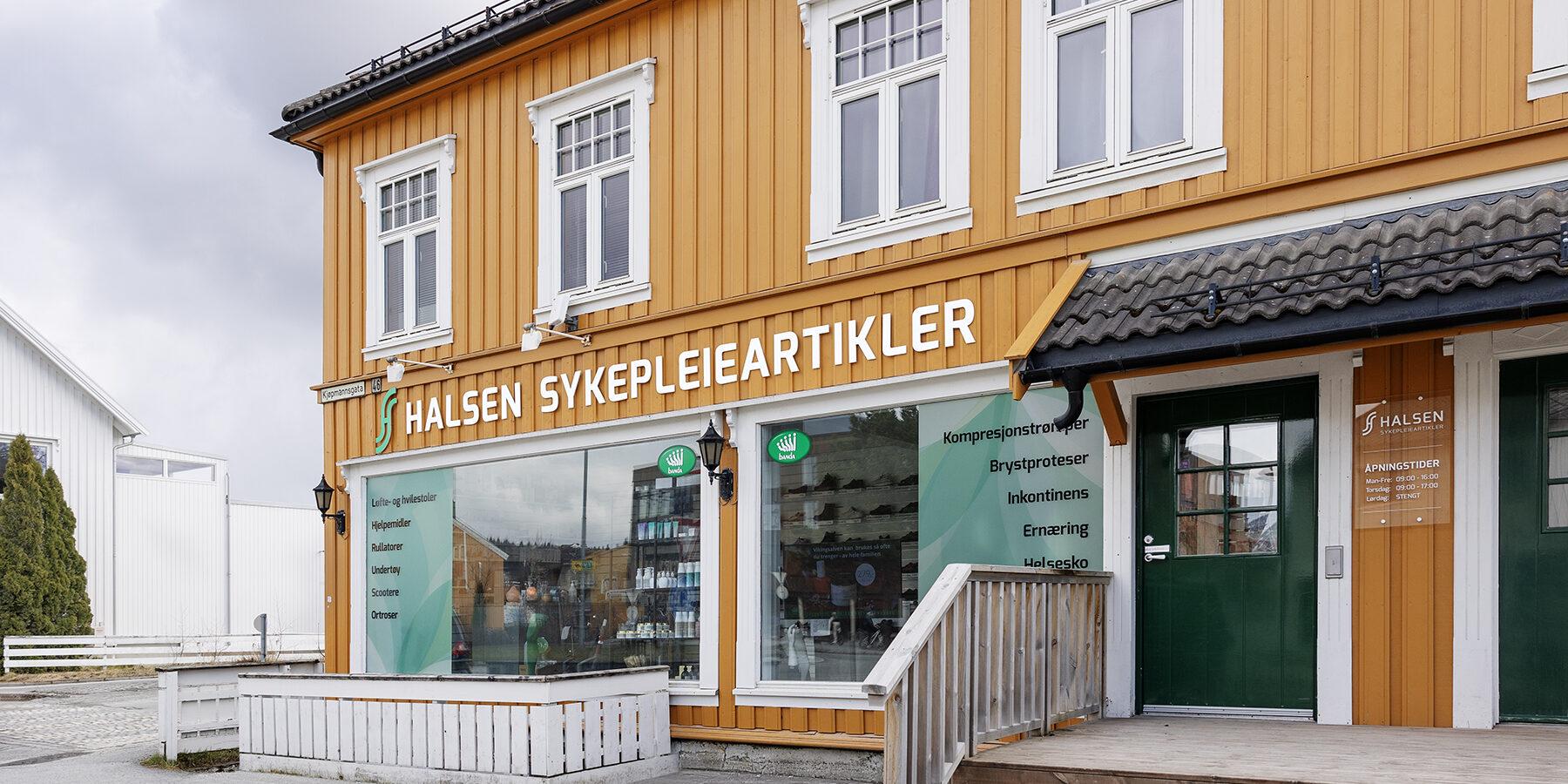 Butikken Halsem Sykepleieartikler med oransje fasade og store vinduer, beliggende i en rolig gate.