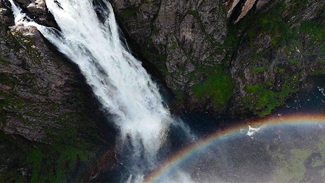 En vakker foss som faller nedover klippene, med en regnbue som danner seg i vannspruten.