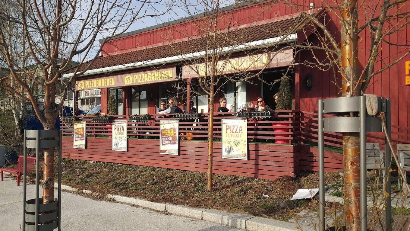 Restaurant med rød fasade og uteservering, omgitt av trær og reklameplakater.