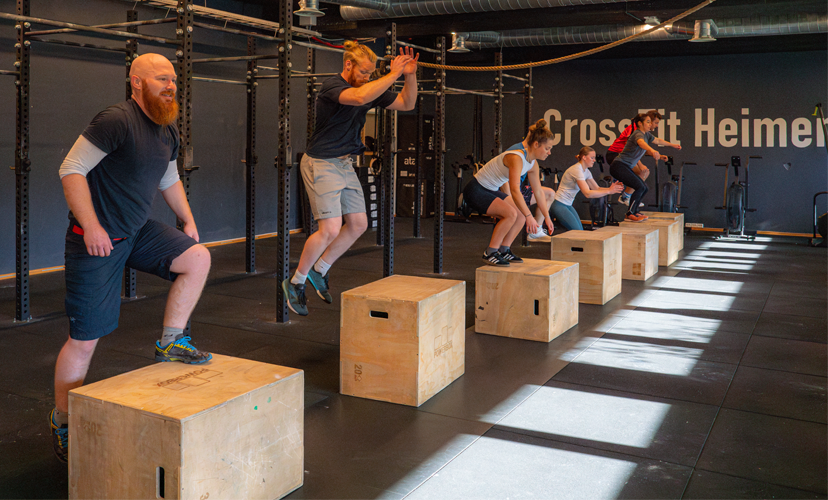 Treningsøkt med fem personer som hopper på kasser i et CrossFit-studio.