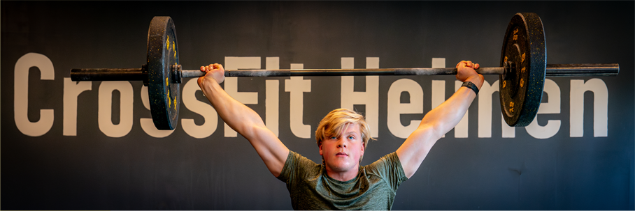 Ung mann løfter en vektstang over hodet i CrossFit Heimen.