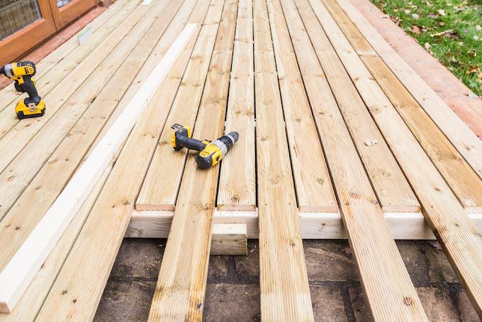 Bilde av en treterrasse med uferdige planker og to boremaskiner på overflaten.