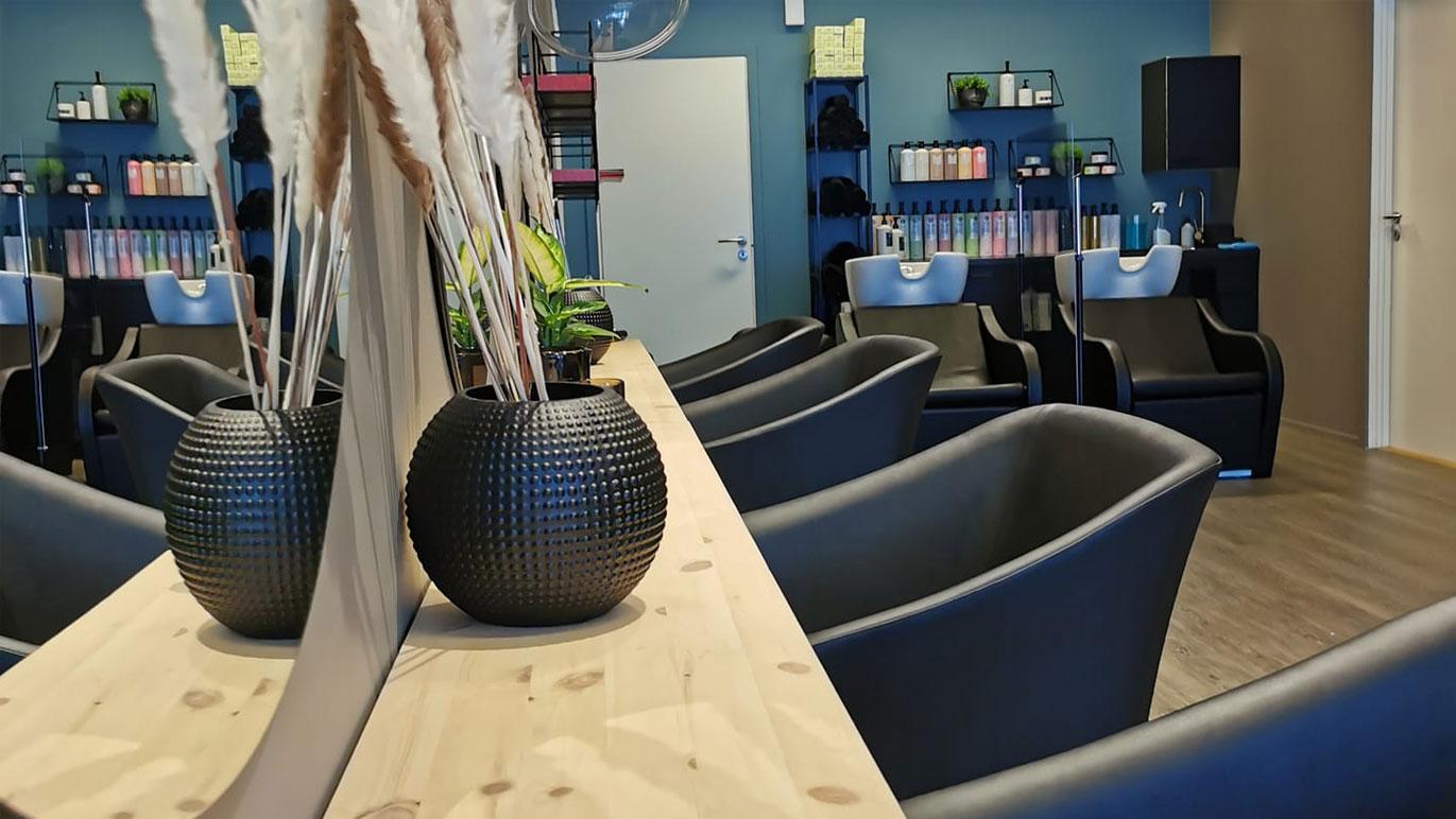Moderne frisørsalong med svarte stoler, en trebenk og dekorative planter i vaser.