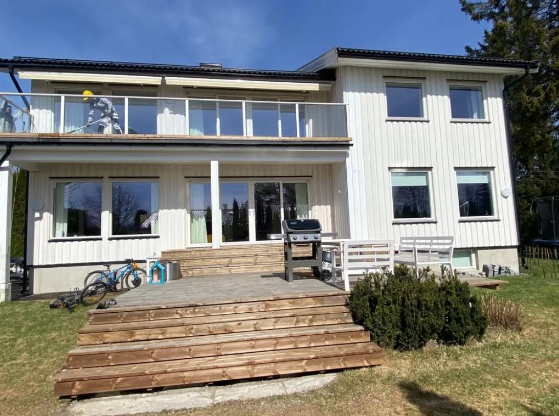 Moderne, hvit enebolig med terrasse og hage, beliggende i et rolig nabolag.