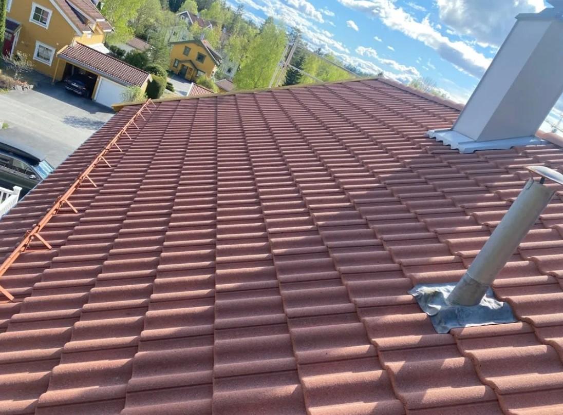Tak med røde takstein og pipe, sett fra oven, med blå himmel og skyer i bakgrunnen.