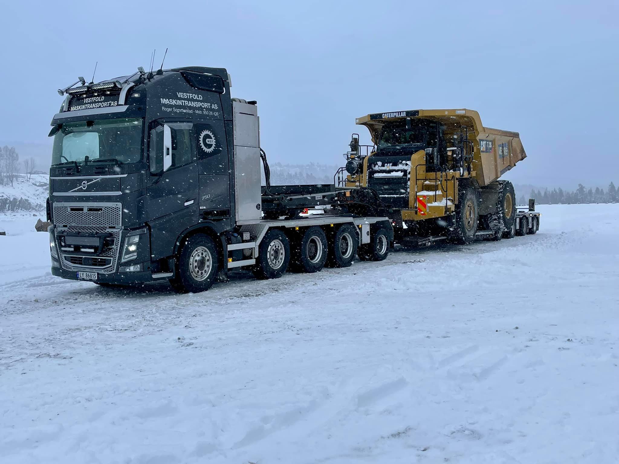En stor lastebil frakter en gruvebil på en snødekt vei i vinterlandskap.