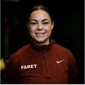 Kvinne med brunt hår iført rød jakke med Nike-logo og teksten "FARET" på brystet.
