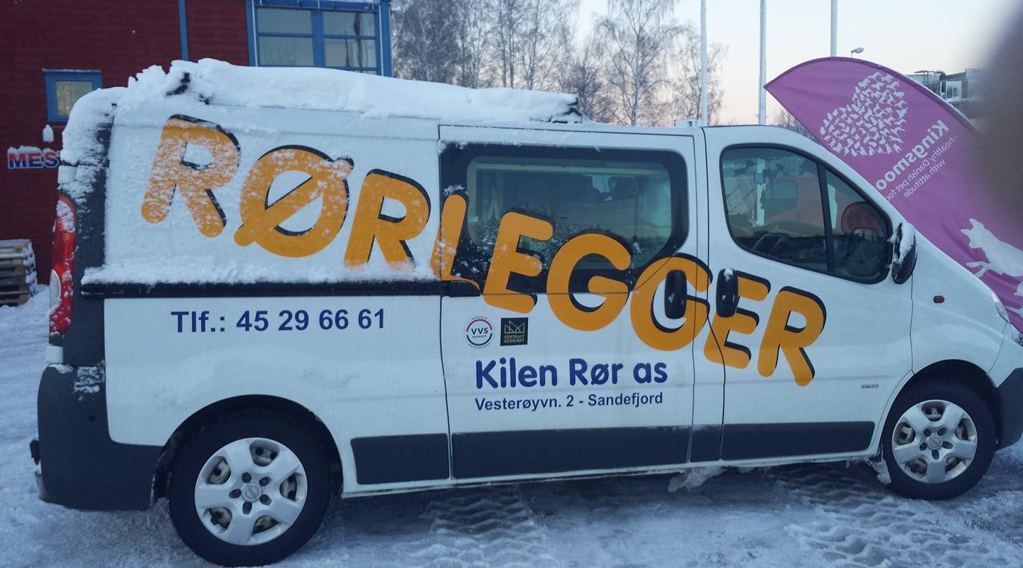 En hvit varebil med snø på taket, merket med "Rørlegger" og kontaktinformasjon på siden.