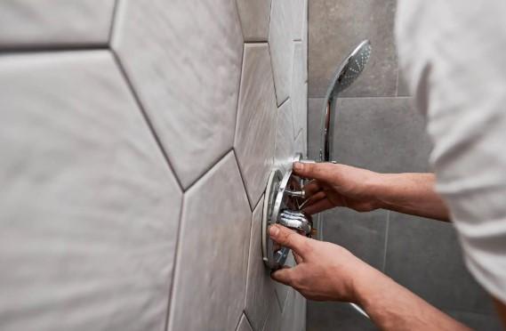 En person installerer en dusjkran på en flislagt vegg med hexagonale fliser.