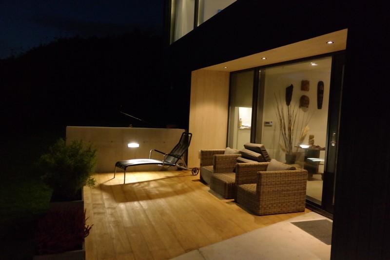 En koselig terrasse med moderne møbler, inkludert en lenestol og sofa, opplyst av myk belysning om kvelden.