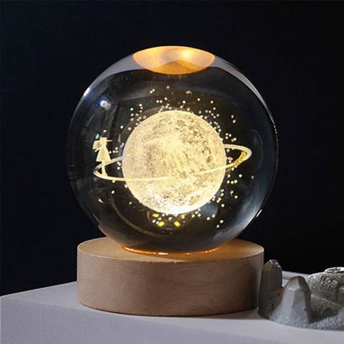 En dekorativ snøglob med en lysende planet og en figur som står på en ring rundt planeten.