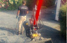 En mann som bruker en gravemaskin på en gruslagt gårdsplass.