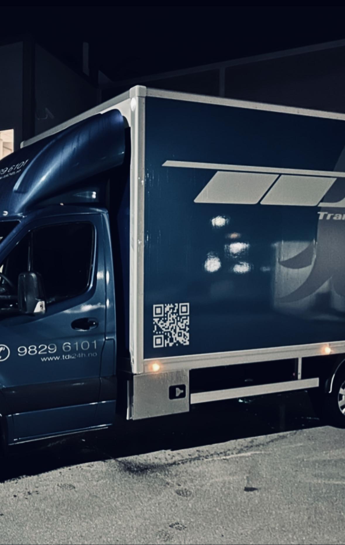 Blå lastebil parkert om natten med QR-kode på siden og lysrefleksjoner på karosseriet.