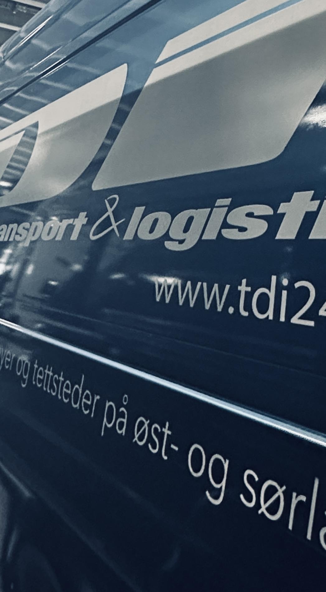 Blå varebil med logo for transport og logistikk, med tekst om tjenester på øst- og sørlandet.