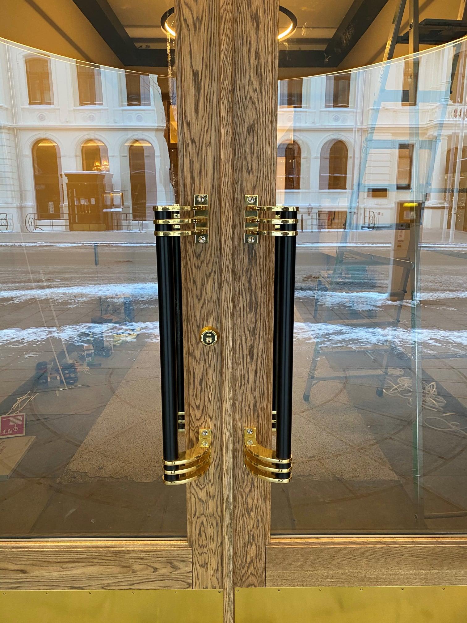 Doble dører med svarte håndtak og gullfargede detaljer, med vindusutsikt mot gaten.