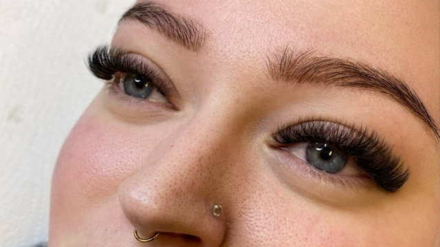 Nærbilde av en kvinne med lange vipper, naturlig sminke og piercing i nesen.