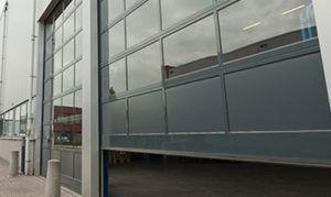 En moderne garasjeport med store vinduer, plassert på en bygning med grå fasade.